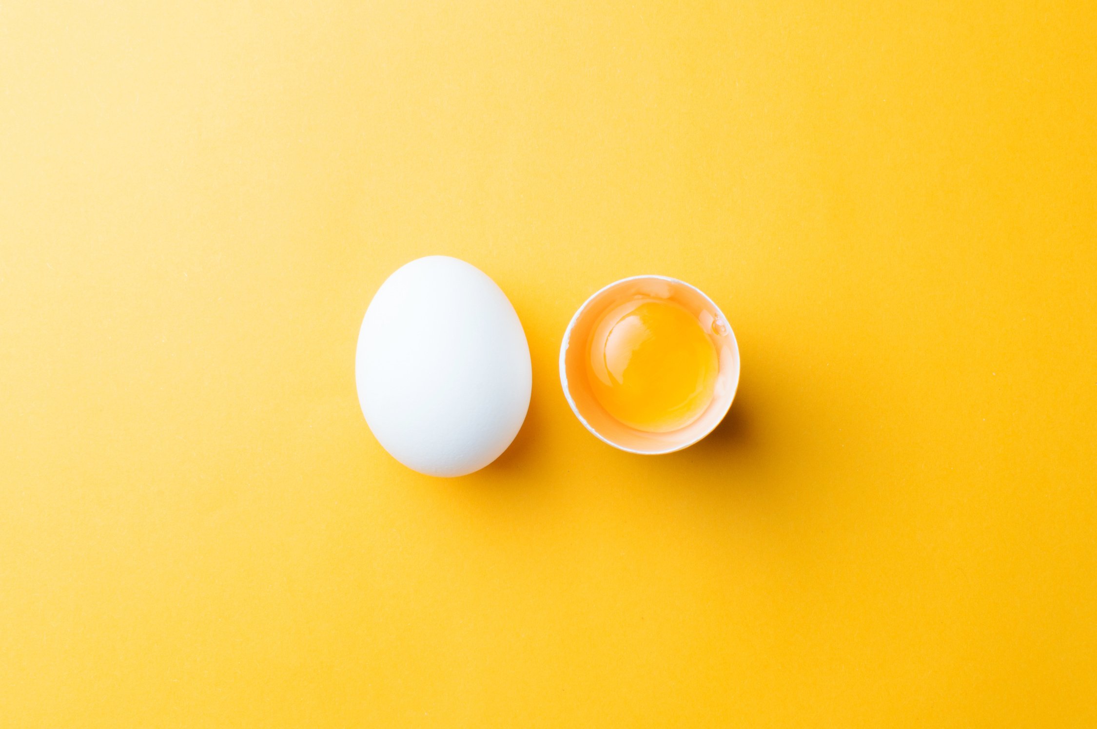 White egg and egg yolk on the yellow background. topview